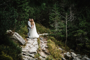 Romantic wedding couple in love standing on the stony shore in forest.