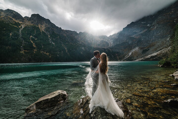 The bride and groom near the lake in the mountains. A couple together against the backdrop of a mountain landscape. Morskie Oko (Sea Eye) Lake. Tatra mountains in Poland. © Serhii
