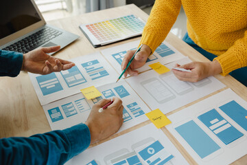 Close up ux developer and ui designer brainstorming about mobile app interface wireframe design on table with customer breif and color code at modern office.Creative digital development agency