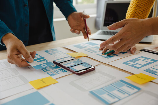 Close up ux developer and ui designer brainstorming about mobile app interface wireframe design on table with customer breif and color code at modern office.Creative digital development agency