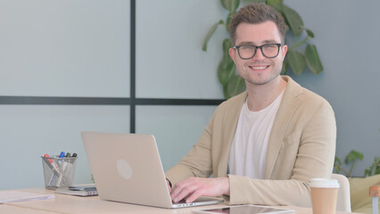 Young Businessman Smiling at Camera while Working on Laptop