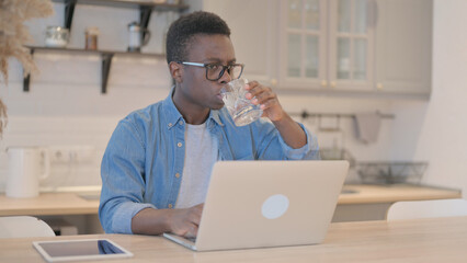 Young Man Drinking Water while Working on Laptop