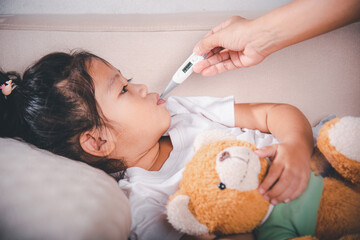 Sick kid. Mother parent checking temperature of her sick daughter with digital thermometer in...