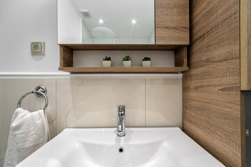Modern light beige bathroom detail, part of white sink, towel besides, wall cabinet with mirros. 