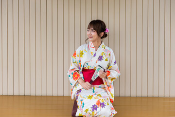 Young woman wearing Japanese traditional kimono holding paper fan sitting in Japanese style wooden...