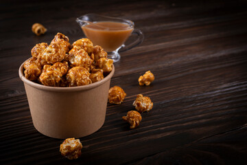 Caramelized popcorn in paper bucket on wooden table