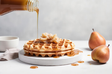 Fresh Belgian waffles with pears are drizzled with liquid caramel syrup. Delicious ruddy waffles stacked on a white plate in a light-colored kitchen. Generative AI professional photo imitation. - obrazy, fototapety, plakaty