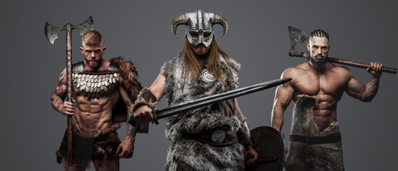 Fototapeta na wymiar Studio shot of muscular vikings dressed in fur and armors armed with axes and swords.
