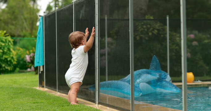 Baby leaning on swimming pool fence protection. Infant standing on safety gate