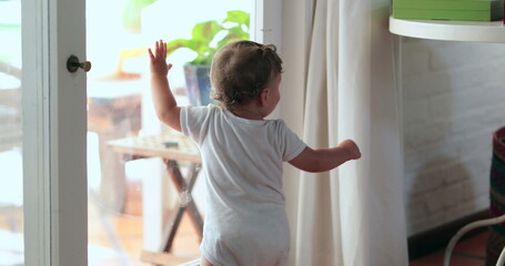Fototapeta na wymiar Baby leaning on home window looking outside