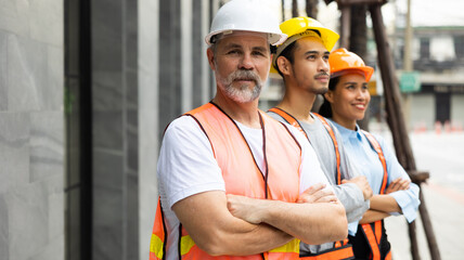 Arms crossed. Unity and teamwork concept. Architect contractor senior man looking at camera and team engineering standing together in construction site. Professional civil engineer team