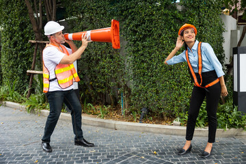 Engineer senior man shouting through traffic cone with girlfriend. funny under construction - obrazy, fototapety, plakaty