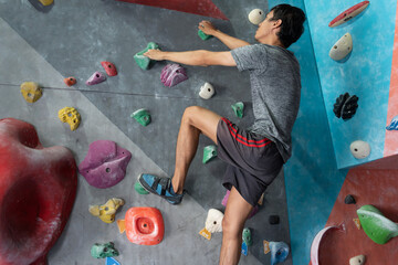 Man climbing on wall training in gym, active sporty male practicing rock climbing on artificial...