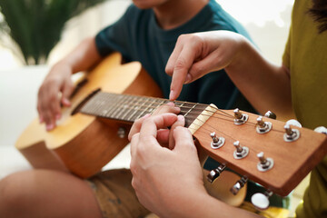 Education concept, learning music. Mother and son playing music together at home. Music teacher teaches young Asian boys how to play guitar - obrazy, fototapety, plakaty