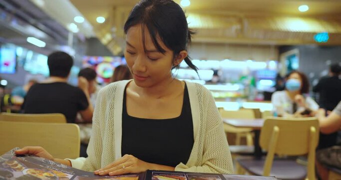 Asian woman sits in a restaurant and opens the menu. She open menu for ordering food in restaurant.