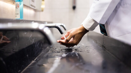 Man washing hand under the water tap on sink in public washroom.