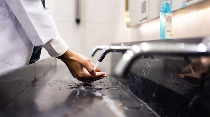 Man washing hand under the water tap on sink in public washroom.