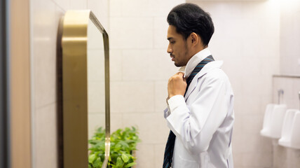 Portrait Asian man doctor getting dressed in restroom looking at mirror at hospital and wellness center. wellness center and hospital. healthcare and medicine