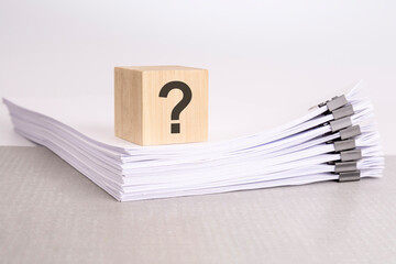 a wooden cube with a question mark on a stack of documents. grey table, white background - obrazy, fototapety, plakaty