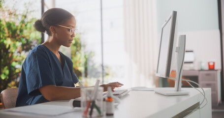 Portrait of a Black Female Medical Health Care Professional Working on Desktop Computer in Hospital Office. Clinic Head Nurse is Appointing Prescriptions Online, Updating Electronic Health Records