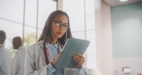 Young Asian Doctor in White Coat Walking and Using a Tablet Computer in Hospital. Beautiful Female Medical Health Care Professional Appointing Prescriptions Online