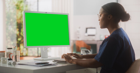 Portrait of a Black Female Medical Health Care Professional Working on Desktop Computer with Green Screen Mock Up Display in Hospital Office. Clinic Head Nurse is Appointing Prescriptions Online