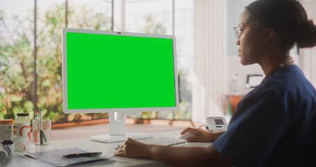 Portrait of a Black Female Medical Health Care Professional Working on Desktop Computer with Green...