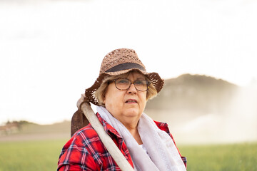 portrait of a grandmother of Caucasian origin wearing a straw hat and red plaid shirt holding her hoe over her shoulder to work in the crop fields.