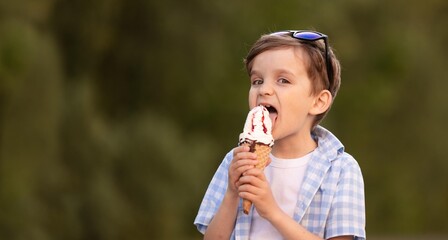 Cute boy 7 years old keeps eating ice cream outdoors in summer