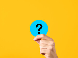 Problem, solution, uncertainty and confusion. FAQ frequently asked questions. Male hand showing a blue circle with question mark symbol on yellow background.