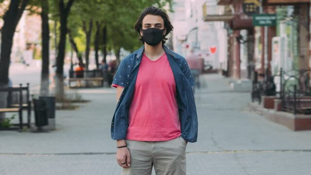 Time Lapse portrait of Middle Eastern person wearing medical mask to prevent covid-19 infection standing in city center alone and looking at camera.