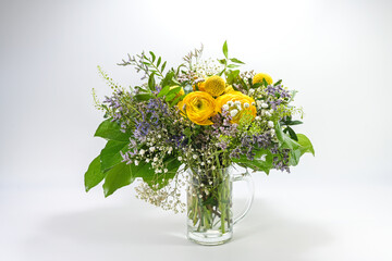 Bouquet from spring flowers in yellow, blue and green in a glass jug against a light gray background with copy space, holiday greeting card