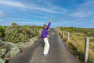 Fototapeta premium Asian woman walking alone on a backpacking trail in Port Campbell National Park. Great Ocean Road, Victoria State, Australia.