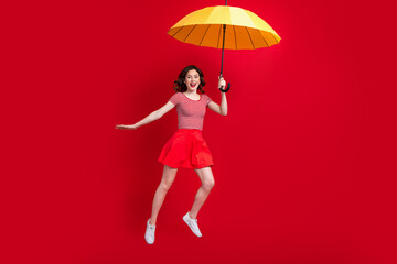 Full body photo of stunning overjoyed lady hand hold umbrella jump flying isolated on red color...