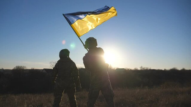 Dolly shot of woman and man in military uniform lifted flag of Ukraine against sunset. Female and male soldier of ukrainian army waving national banner at countryside. Resistance to russian invasion
