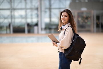 Obraz premium Positive young asian lady student with backpack, tablet in wireless headphones ready for lesson in university