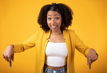Happy young black lady showing thumbs down to empty space, isolated on yellow background, ad and...