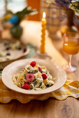 Tasty pasta with spinach and berries decorated with edible flowers on dining table