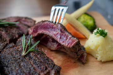 Medium rare meat on fork with wooden plate on the background