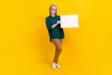 Full length portrait of positive lady hands hold showing empty space paper blank isolated on yellow color background