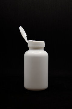 empty white medicine bottle with opem lid on the black background