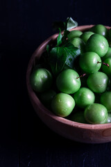 Fresh green plums in a bowl on dark background.