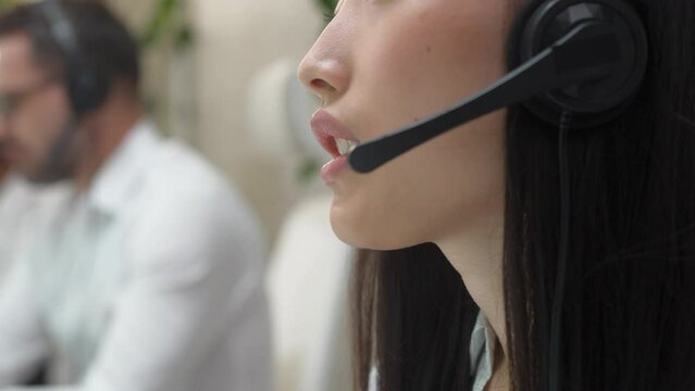 Close-up of Asian female operator with headset consulting client. Young woman supporting customer in office. In blurren background visible busy coworkers. Call-center service. Financial industry.