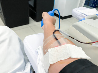 Blood platelet donation, a male nurse inserts a needle into donor’s arm to draw blood at a...
