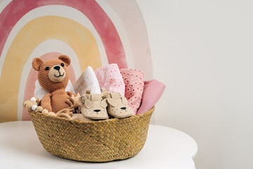 Basket with baby stuff and accessories for newborn. Gift basket with cotton clothes and muslin swaddle blanket, baby shoes, toys and cute teddy bear in beige colors. - obrazy, fototapety, plakaty