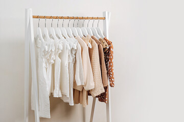 Clothing Rack with children's outfits close up. Fashion clothes in white, beige and brown colors on hangers in wardrobe. Kids wardrobe. Set of kids clothes and accessories.