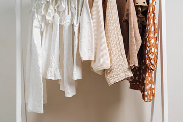 Clothing Rack with children's outfits close up. Fashion clothes in white, beige and brown colors on hangers in wardrobe. Kids wardrobe. Set of kids clothes and accessories.