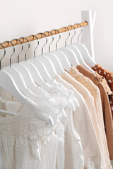 Clothing Rack with children's outfits close up. Fashion clothes in white, beige and brown colors on hangers in wardrobe. Kids wardrobe. Set of kids clothes and accessories.