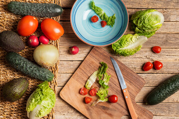 Vegetables and fruits next to a bowl and a cutting board to prepare a salad, on a rustic wooden background.