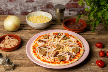 Plate with a pizza ready to bake, with vegetables, tuna, cooked ham and anchovies, close-up.